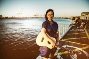 Portraitfoto von Prita mit Gitarre am Meer