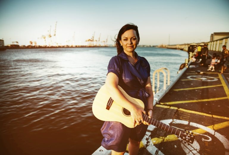 Portraitfoto von Prita mit Gitarre am Meer